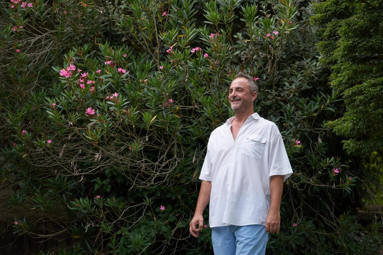 Fabio Semenzato cammina sorridendo davanti a un grande oleandro fiorito