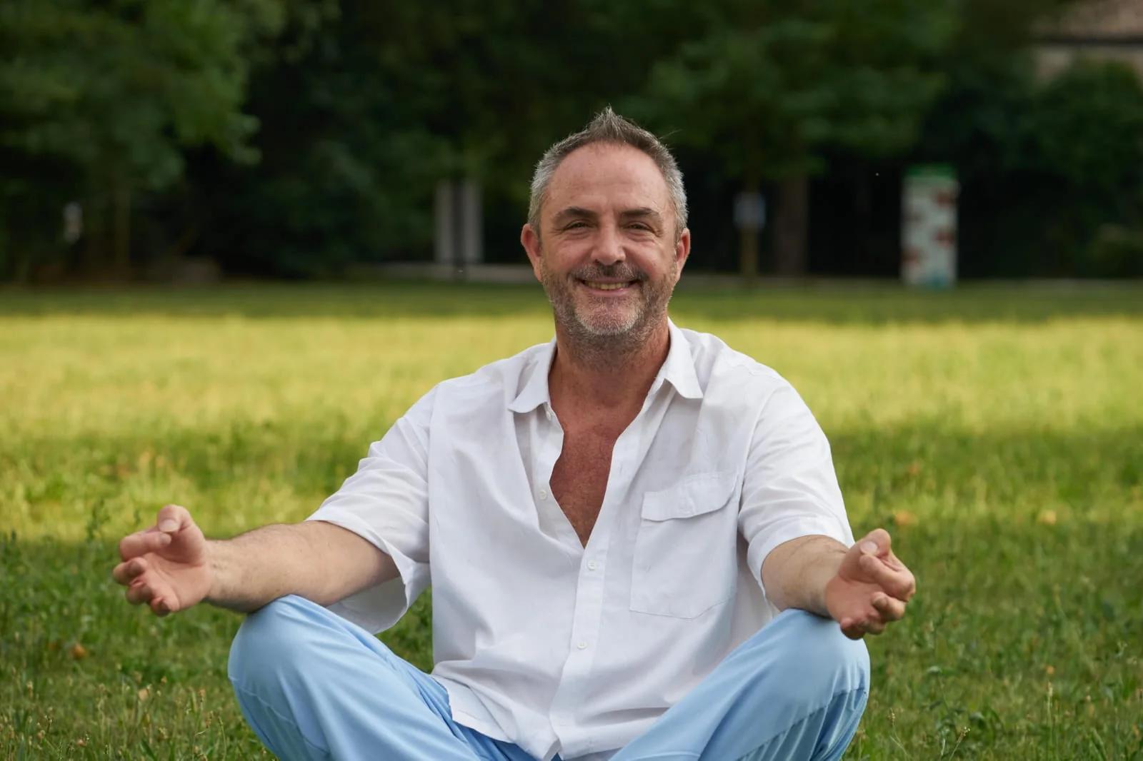 Fabio Semenzato seduto a gambe incrociate su un prato, in meditazione, sorridente